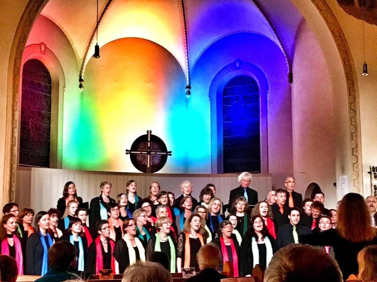 Die Rainbow Gospel Voices singen in einer mit Regenbogenfarben beleuchteten Kirche.